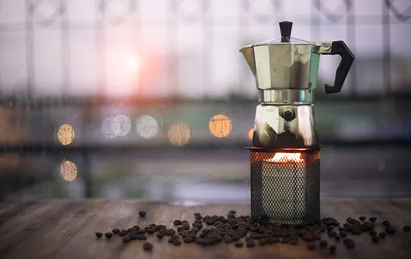 mocha pot on wooden table with roasted coffee beans by window