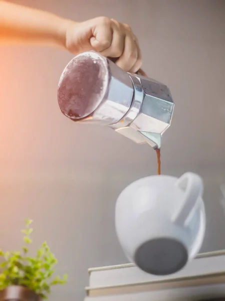 hand pouring coffee from coffee pot in cup