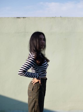 Parlak güneş ışığında poz veren çizgili kazaklı genç kadın.