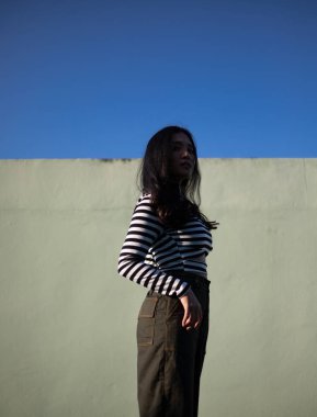 Parlak güneş ışığında poz veren çizgili kazaklı genç kadın.