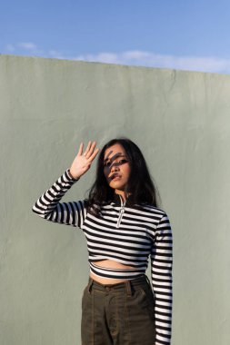 Parlak güneş ışığında poz veren çizgili kazaklı genç kadın.