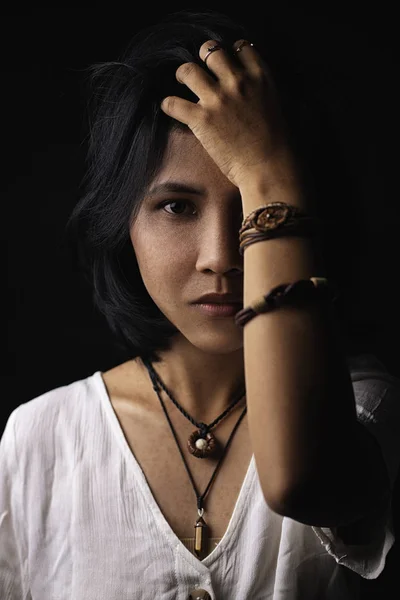 Asian short black haired woman Wearing jewelry made of leather and stone On her face, there is a small freckle On a black background and shadows