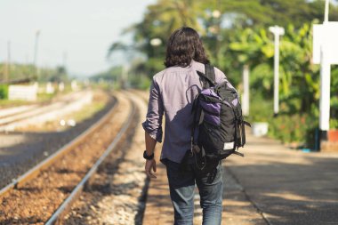 Serin görünüyor Uzun saçlı adam O sırt çantasıyla ve gitar bir gezgin ya da göçebe müzisyen, kırsal tren yolu yakınında yürüyor.