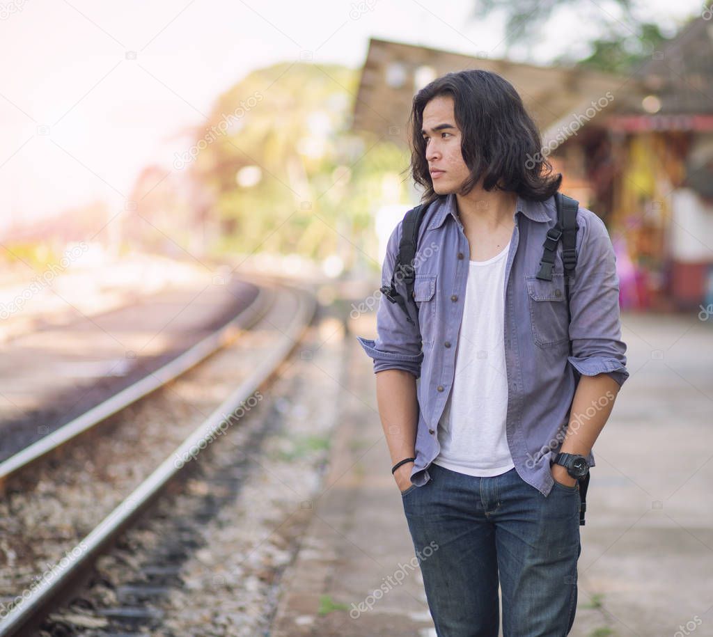 Long haired man that looks cool He is a traveler or nomadic musician who is backpacking and guitars, walking near train track in rural.