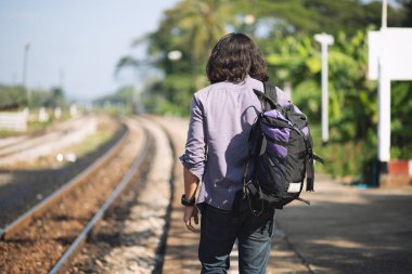 Serin görünüyor Uzun saçlı adam O sırt çantasıyla ve gitar bir gezgin ya da göçebe müzisyen, kırsal tren yolu yakınında yürüyor.