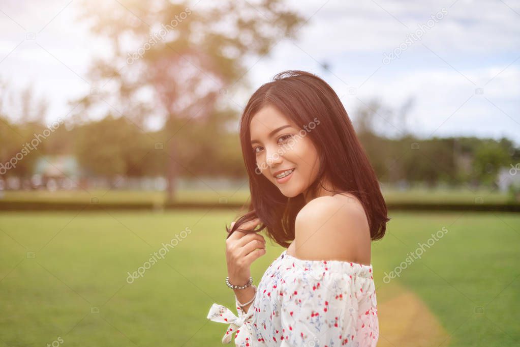 A beautiful Japanese woman wearing a white dress, walking happily in the green lawn. In the light of the sun