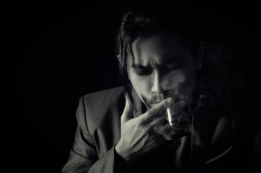 Uzun saçlı, takım elbiseli bir iş adamı karanlıkta dönen sandalyeyi düşünüyor..