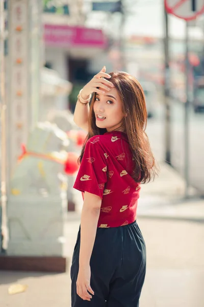 Hatyai, Thailand - Feb 3, 2020: Brown long haired girl Wearing a red T-shirt and Nike warm pants on a casual day, she is walking in a sunny city.