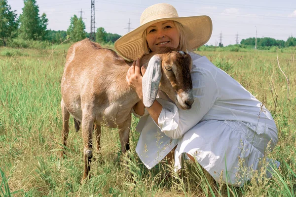 Gülümseyen bir kadın çiftçi bir Nubian keçisine sarılıyor..