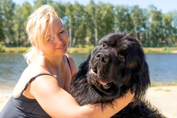 Bir kadın sahilde büyük bir köpeğe sarılıyor..