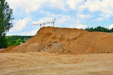Kum ve yeni ev yapımı yığını. Sanayi için kavram. Bulutlar ve güneş ile vinç ve mavi gökyüzü. Bina inşaat alanında günbatımı