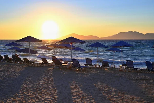 Sunbeds and umbrella on the beach at sunset by the sea. Beautiful concept for vacation, summer holidays and travel. — Stock Photo, Image