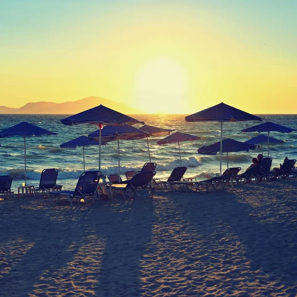 Sunbeds and umbrella on the beach at sunset by the sea. Beautiful concept for vacation, summer holidays and travel. — Stock Photo, Image