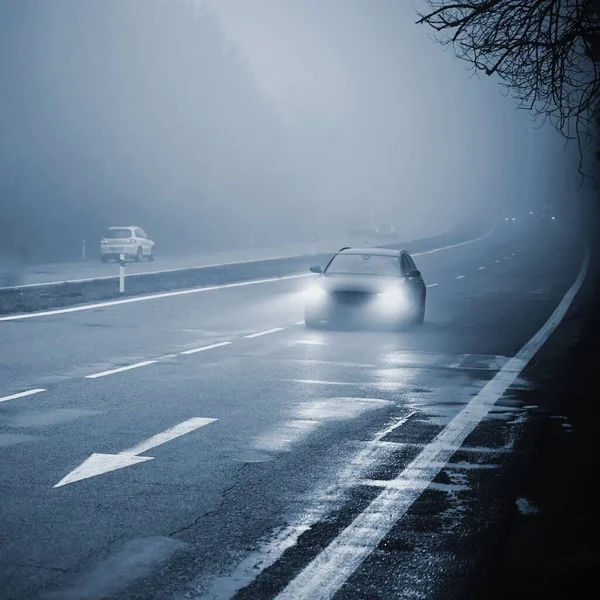 Carros no nevoeiro. Mau tempo de inverno e tráfego automóvel perigoso na estrada. Veículos leves em dia nebuloso . — Fotografia de Stock