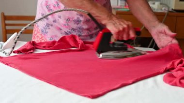 Yaşlı bir kadın eski bir ütüyle giysileri ütülüyor ve onları evde katlıyor. Ev işleri ve retro konsept.