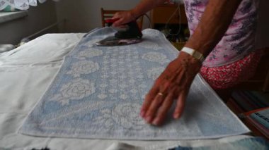 Yaşlı bir kadın eski bir ütüyle giysileri ütülüyor ve onları evde katlıyor. Ev işleri ve retro konsept.