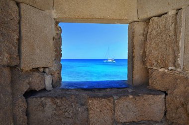 Antik duvardan deniz manzarası, seyahat ve tatil konsepti. Turkuaz deniz ve yelkenli yaz tatili. Okyanusa açılan taş pencere. Deniz. Rodos Adası Yunanistan - Eski kentteki kale.