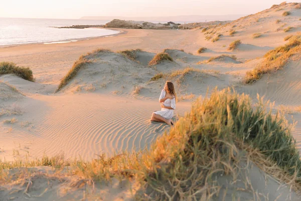 Retrato de jovem mulher feliz em vestido branco, encontra-se nas dunas de areia ao lado do mar. em horário de verão, ao pôr do sol . — Fotografia de Stock