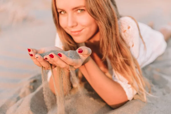 Portrét šťastné mladé ženy v bílých šatech, leží na písečných dunách u moře. v létě, při západu slunce. — Stock fotografie