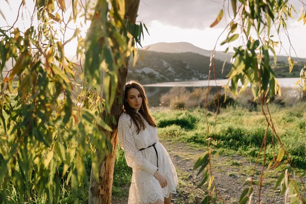 Młoda, urocza dziewczyna w białej sukience i czarnym kapeluszu, wiosną, pozująca do kamery. Portret kobiety na świeżym powietrzu w górskim jeziorze. Zielona świeża trawa. Młoda niezwykła osoba ciesząca się naturą — Zdjęcie stockowe