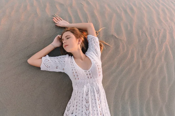 Portrait de jeune femme heureuse en robe blanche, se trouve sur les dunes de sable à côté de la mer. en été, au coucher du soleil . — Photo