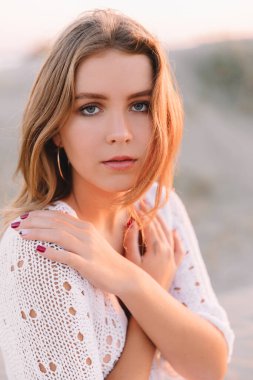 Beyaz elbiseli bir kız yazın, gün batımında sahilde yürüyor ve eğleniyor. Denizde mutlu genç bir kadının portresi.