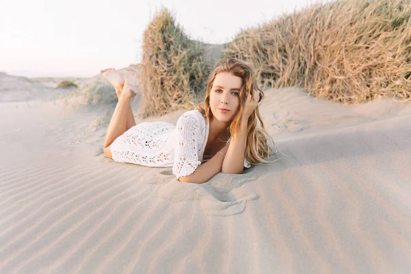 Portrait de jeune femme heureuse en robe blanche, se trouve sur les dunes de sable à côté de la mer. en été, au coucher du soleil . — Photo