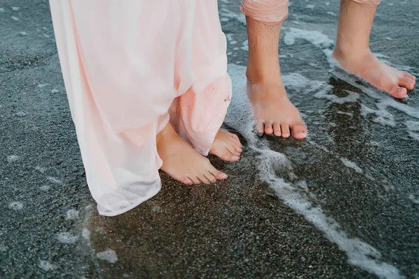 Bride and groom walking on the beach barefoot stepping in the water — Stock Photo, Image