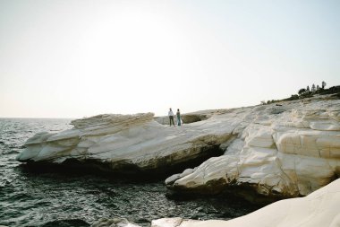 Arka plan, okyanusun önündeki kayalıklarda duran evli bir çift. Sadece arkadan evlilik manzarası. Denizde balayı.