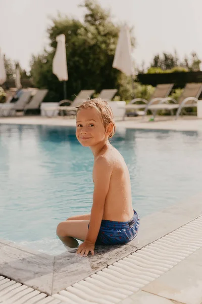 Enfant garçon est assis près d'une piscine extérieure en été. Week-end en famille en chalet d'été — Photo