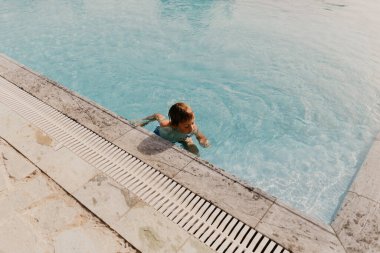 Çocuk yazın havuzda yüzer.