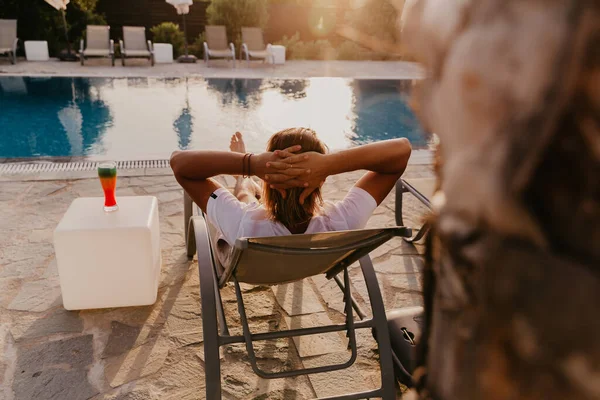 カクテルを飲みながらプールのそばのラウンジャーに寝そべってる若い男。夏休み — ストック写真
