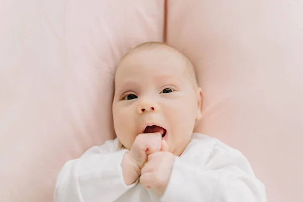 Niña acostada en la cama mordisqueando sus puños — Foto de Stock