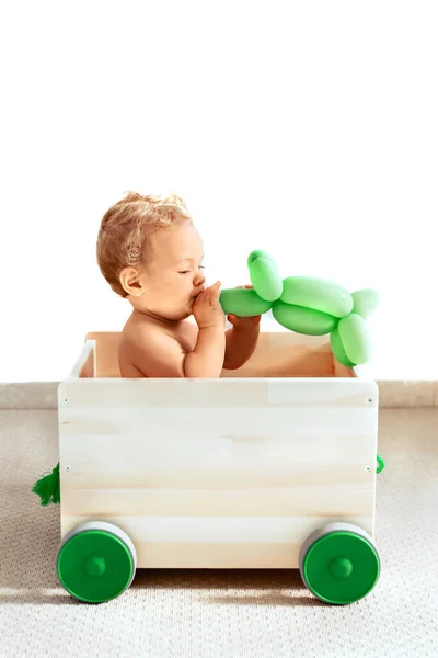 Niña con globo verde en una caja de juguetes sobre un fondo blanco, aislada . — Foto de Stock