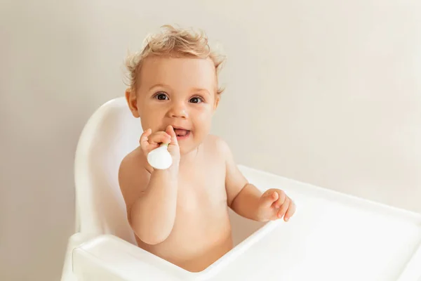 Niña feliz sentada en una silla alta y sosteniendo una cuchara en su boca . — Foto de Stock