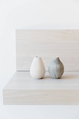 Beyaz ahşap bir rafta iki kil vazo..
