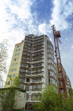 Mavi gökyüzünün arka planında yapım aşamasındaki çok katlı bir bina ve vinç.