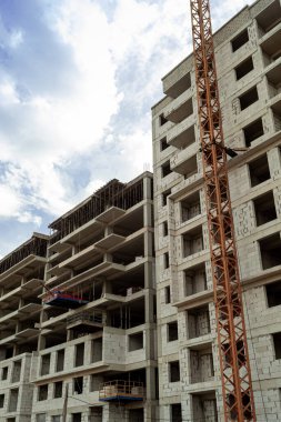 Mavi gökyüzünün arka planında yapım aşamasındaki çok katlı bir bina ve vinç.