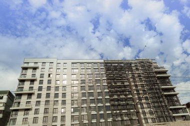 Mavi gökyüzünün arka planında yapım aşamasındaki çok katlı bir bina ve vinç.