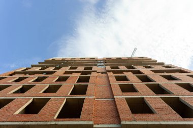 Mavi gökyüzünün arka planında yapım aşamasındaki çok katlı bir bina ve vinç.