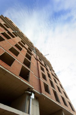 Mavi gökyüzünün arka planında yapım aşamasındaki çok katlı bir bina ve vinç.