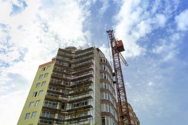Mavi gökyüzünün arka planında yapım aşamasındaki çok katlı bir bina ve vinç.