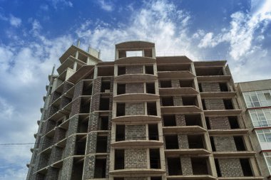 Mavi gökyüzünün arka planında yapım aşamasındaki çok katlı bir bina ve vinç.