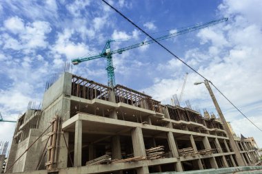 Mavi gökyüzünün arka planında yapım aşamasındaki çok katlı bir bina ve vinç.