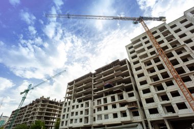 Mavi gökyüzünün arka planında yapım aşamasındaki çok katlı bir bina ve vinç.