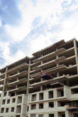 Mavi gökyüzünün arka planında yapım aşamasındaki çok katlı bir bina ve vinç.