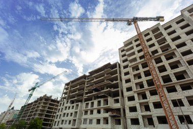 Mavi gökyüzünün arka planında yapım aşamasındaki çok katlı bir bina ve vinç.