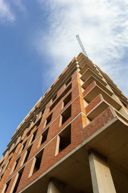 Mavi gökyüzünün arka planında yapım aşamasındaki çok katlı bir bina ve vinç.