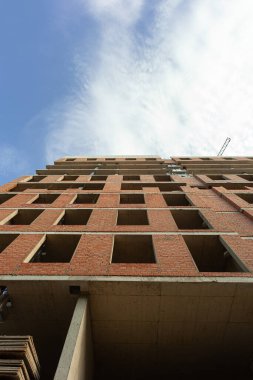 Mavi gökyüzünün arka planında yapım aşamasındaki çok katlı bir bina ve vinç.