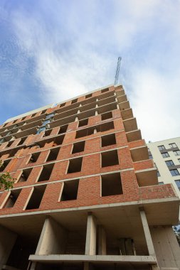 Mavi gökyüzünün arka planında yapım aşamasındaki çok katlı bir bina ve vinç.